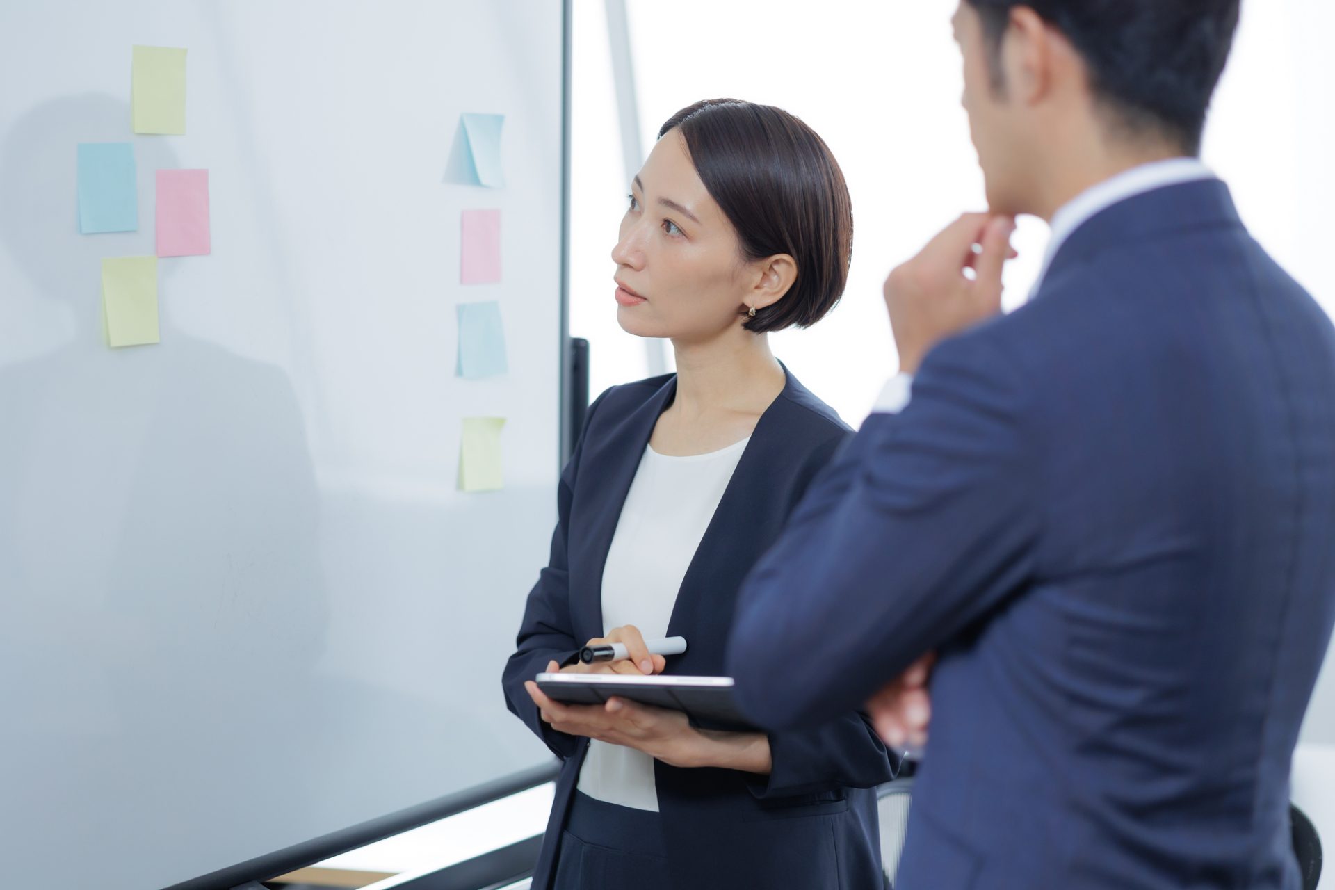 ホワイトボードの前で話し合うスーツ姿の男女
