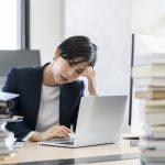 ノートパソコンの画面を見ながら頭を抱えるビジネスウーマン